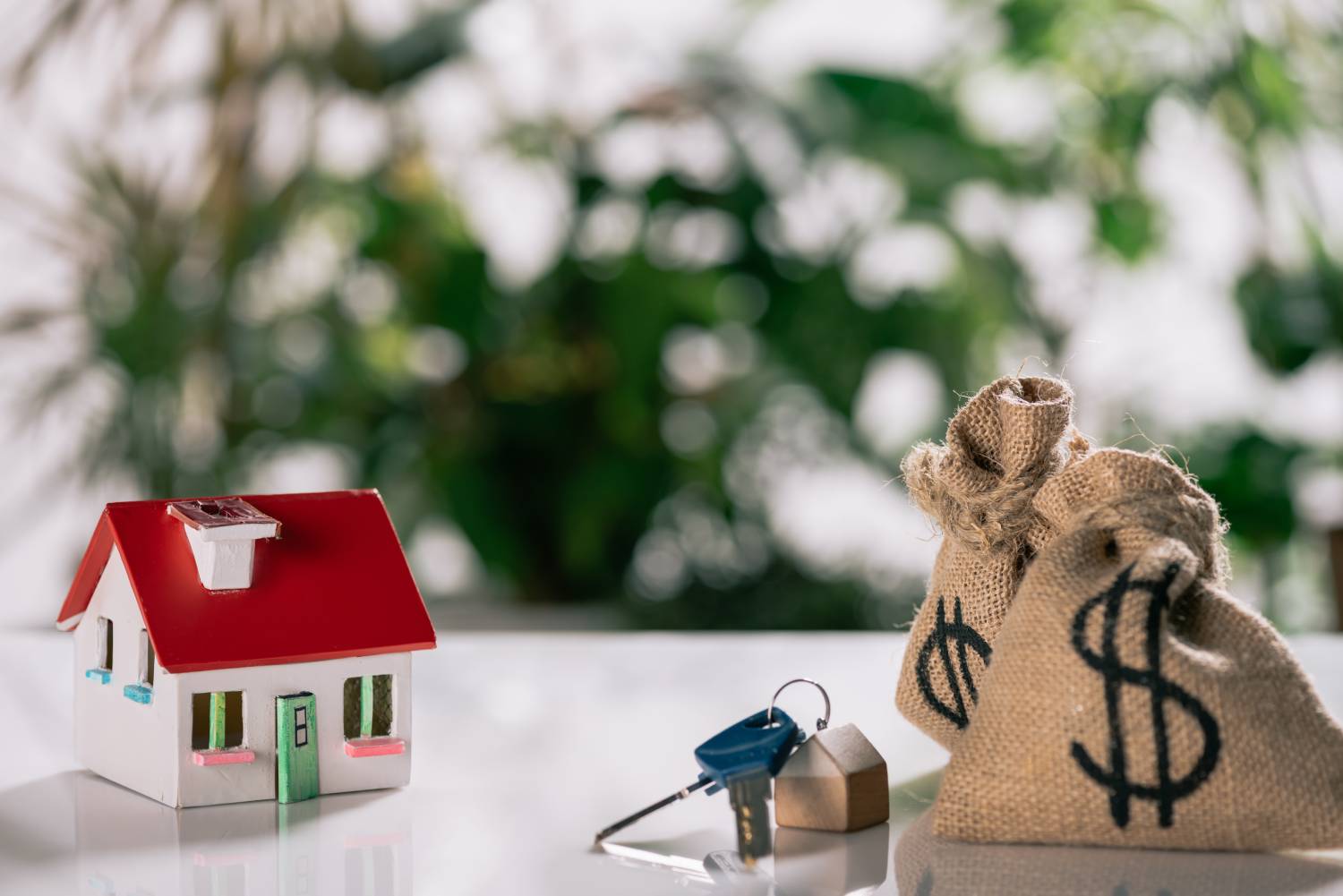 Miniature house model with keys and money bags symbolizing foreclosure funds recovery and real estate equity.